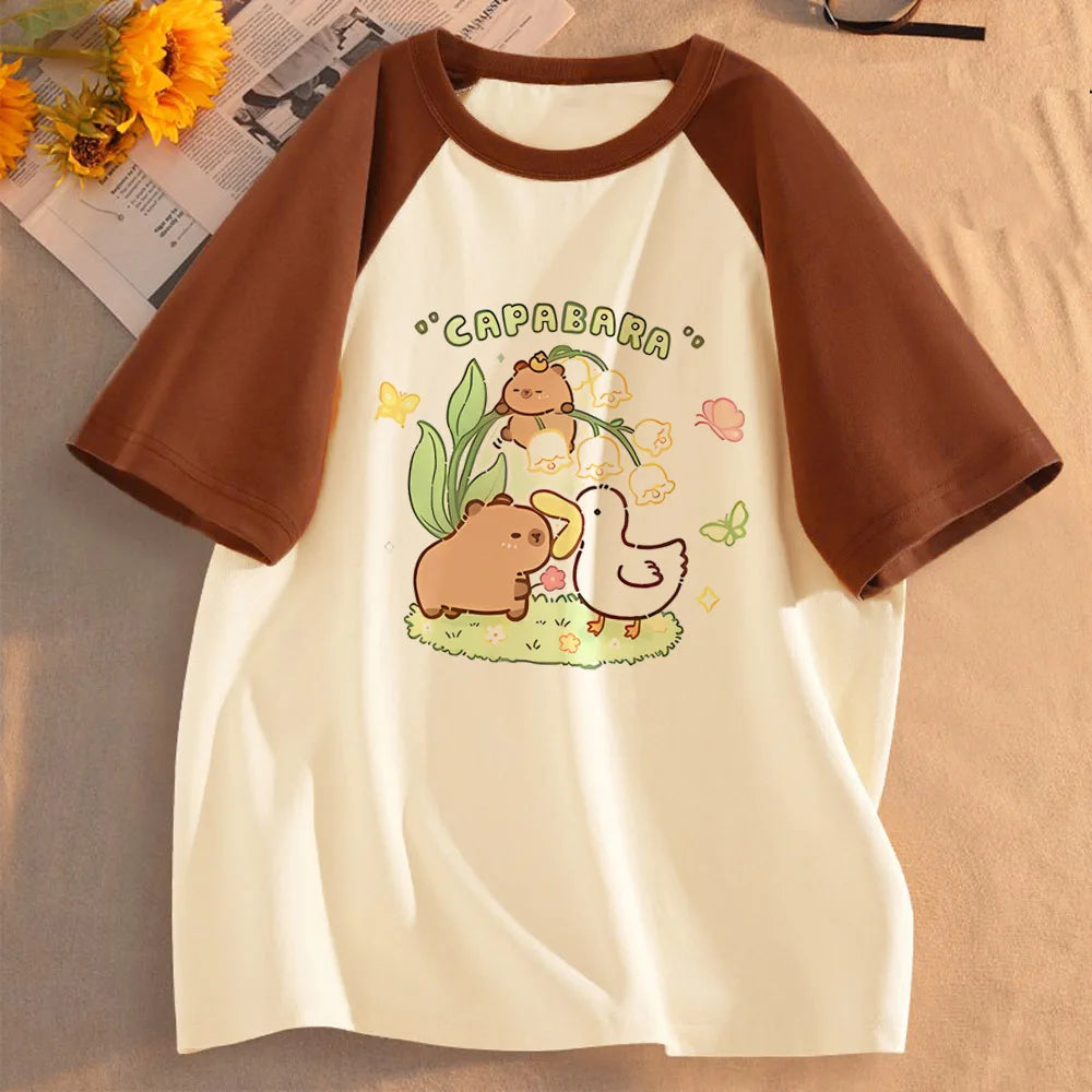 Beige T-Shirt mit grafischer Darstellung von zwei Capybaras auf grünen Blättern.