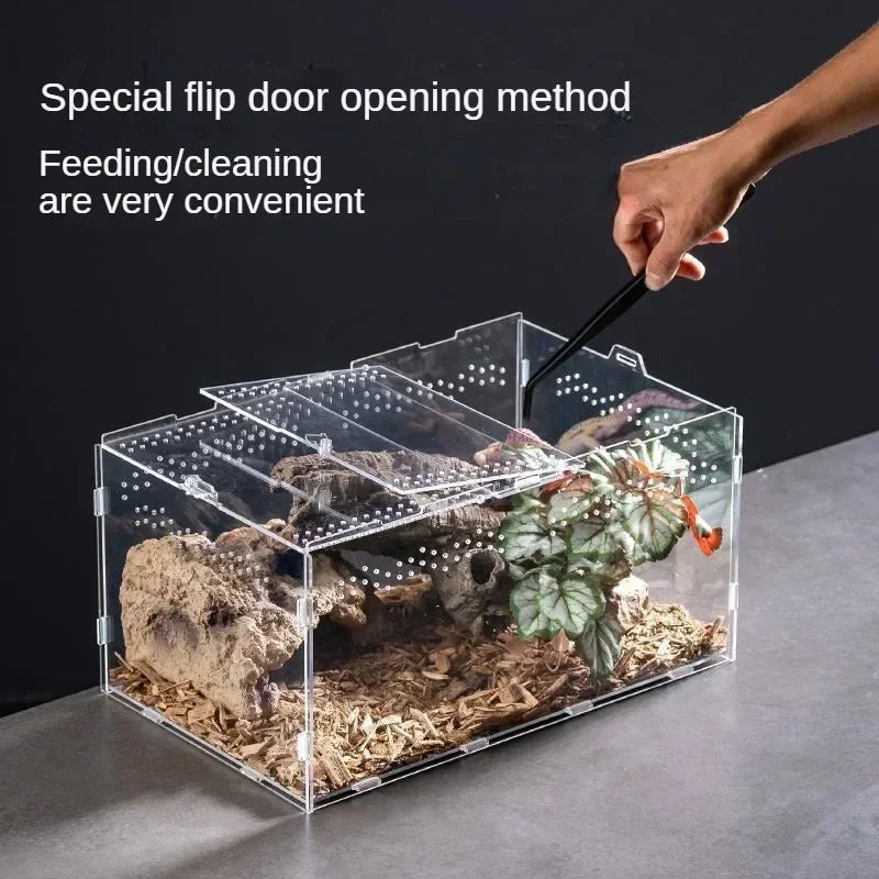 A hand is using a tool to open the flap door of a transparent acrylic reptile terrarium for feeding or cleaning.