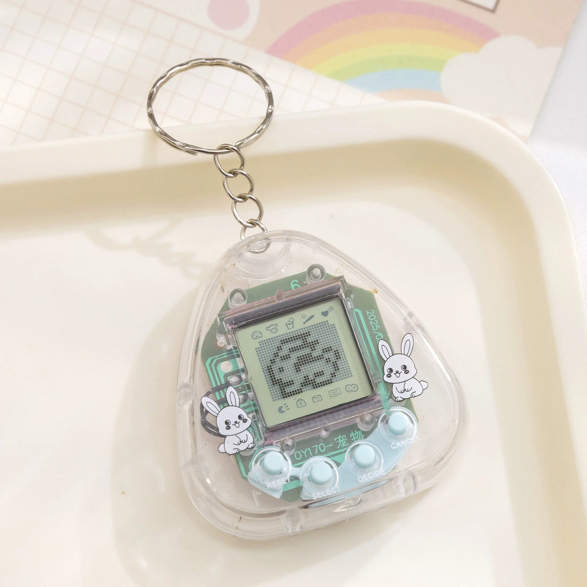 A clear plastic digital pet toy with a metal keyring attached, featuring an LCD screen and a small rabbit design.