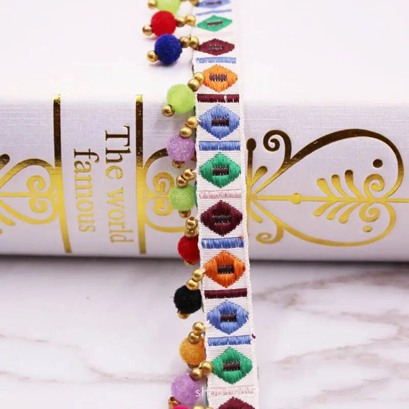 Close-up of a white fabric with a gold trim featuring colorful pearl pom poms and lace for sewing crafts