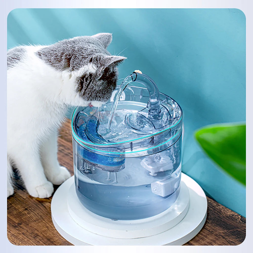 A white and gray cat looks at a blue pet water fountain with water flowing.