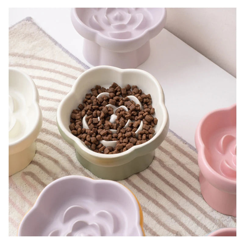 A collection of ceramic slow feeder bowls for pets, including a brown textured bowl and pink bowls, set on a light fabric.