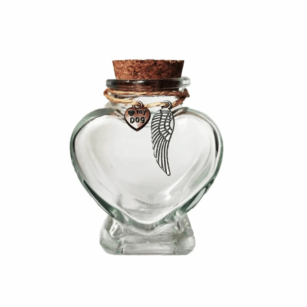 A clear glass heart-shaped jar with a cork stopper and a silver pendant shaped like a dog's head and wings.