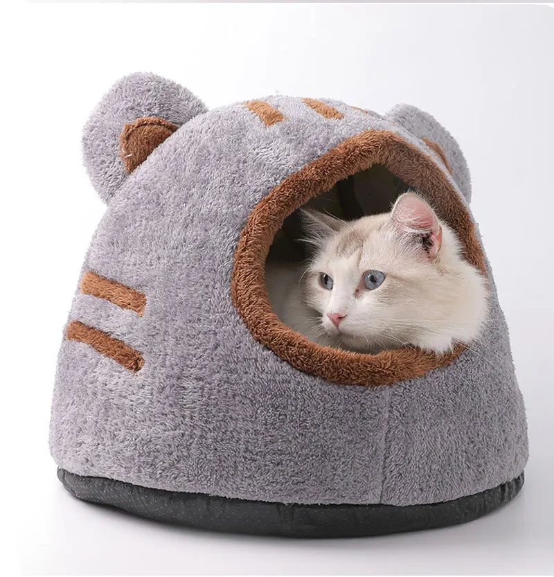Graues, flauschiges Katzenbett in Form eines Tigerkopfes mit Öffnung, die eine weiße Kätzchen zeigt.