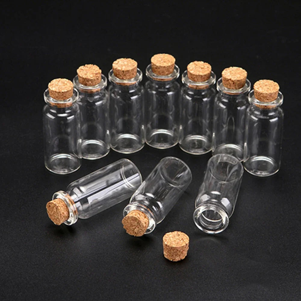 A collection of ten mini glass bottles with cork stoppers arranged on a dark surface.