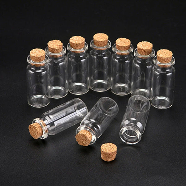 A collection of ten mini glass bottles with cork stoppers arranged on a dark surface.