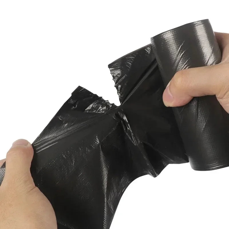 A hand is holding a black disposable plastic garbage bag with tie handles.