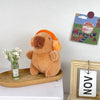 Flauschiges braunes Capybara-Plüschtier auf einem Holzbrett neben einem gerahmten Kunstwerk.