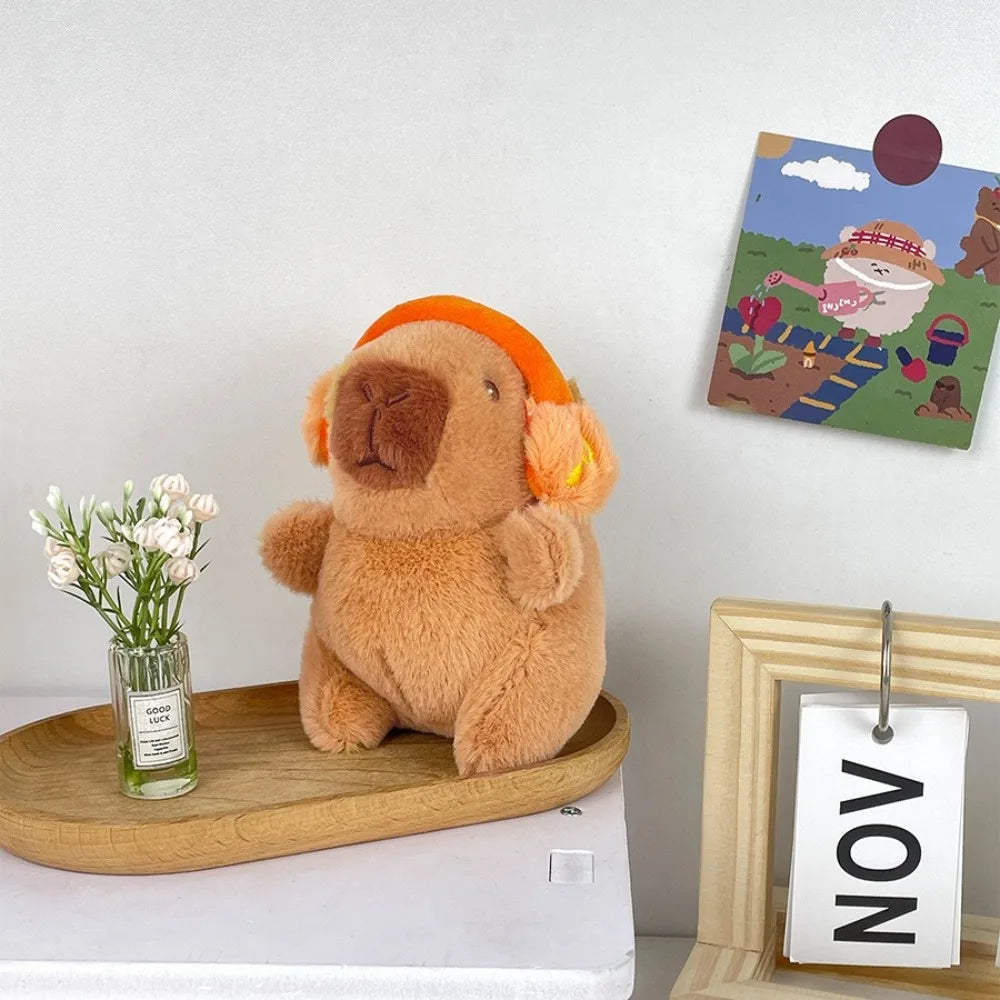 Flauschiges braunes Capybara-Plüschtier auf einem Holzbrett neben einem gerahmten Kunstwerk.