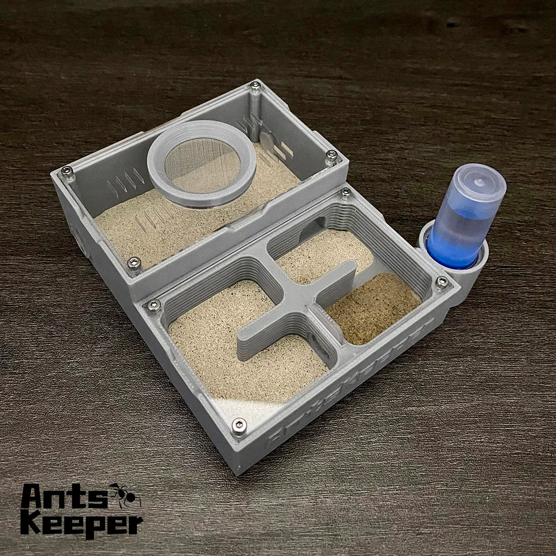 A gray plastic four-chamber ant observation farm with various compartments and a blue liquid sample.