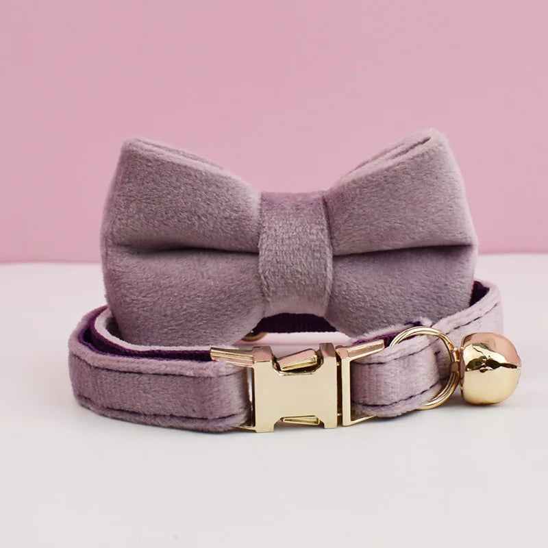 A lavender velvet cat collar with a bow and gold hardware displayed on a white surface.