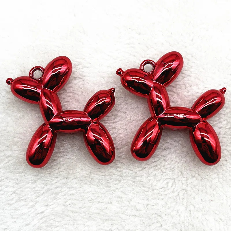 A pair of shiny red acrylic balloon dog charm pendants resting on a white, textured surface.