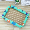 A rectangular pet bed with a green fabric border featuring orange and blue animal faces, lined with a woven rattan mat.