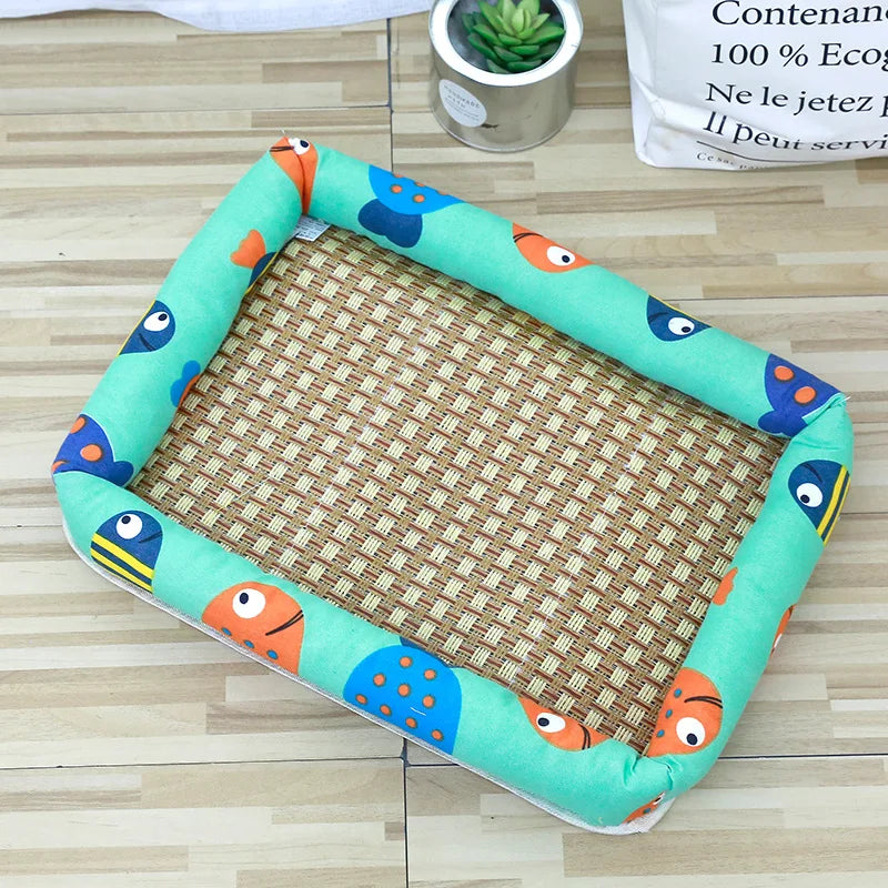 A rectangular pet bed with a green fabric border featuring orange and blue animal faces, lined with a woven rattan mat.