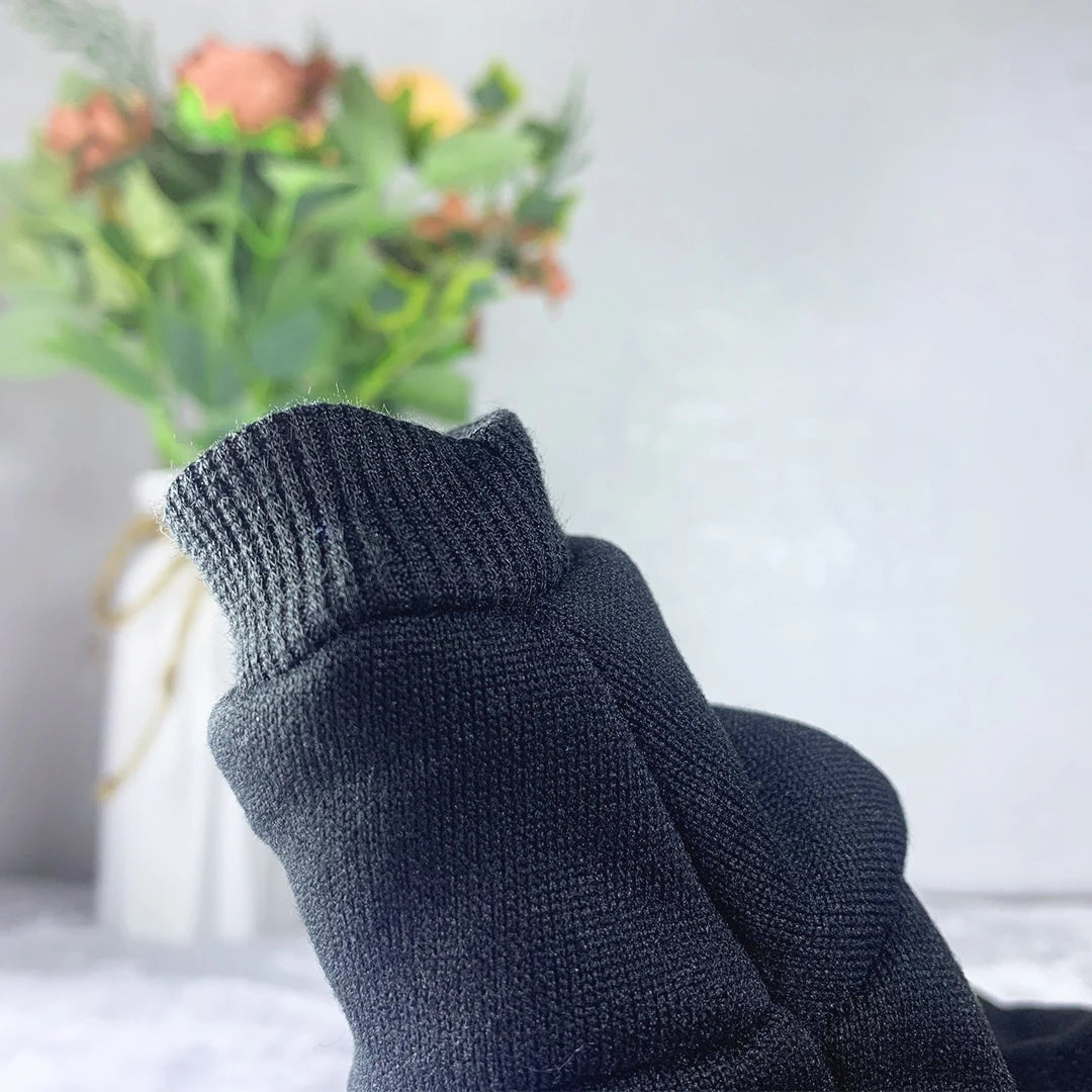 A close-up of a dark gray knitted dog hoodie sweatshirt with a ribbed cuff, resting in front of a blurred floral arrangement.