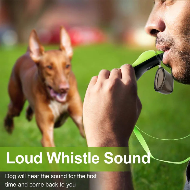 A person is blowing a green whistle towards a dog in a grassy outdoor setting.