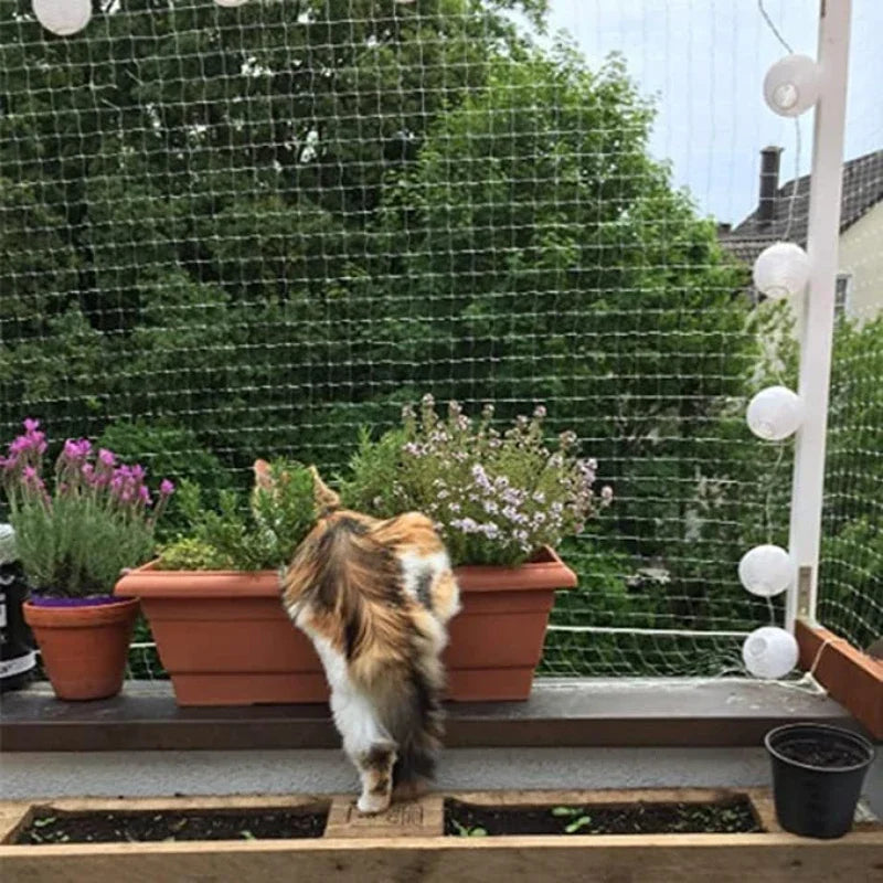 A cat window safety net is installed on a balcony railing, with potted plants and a small garden bed below.