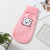 A pink knitted sweater for a small dog with a white paw print design, resting on a white surface.
