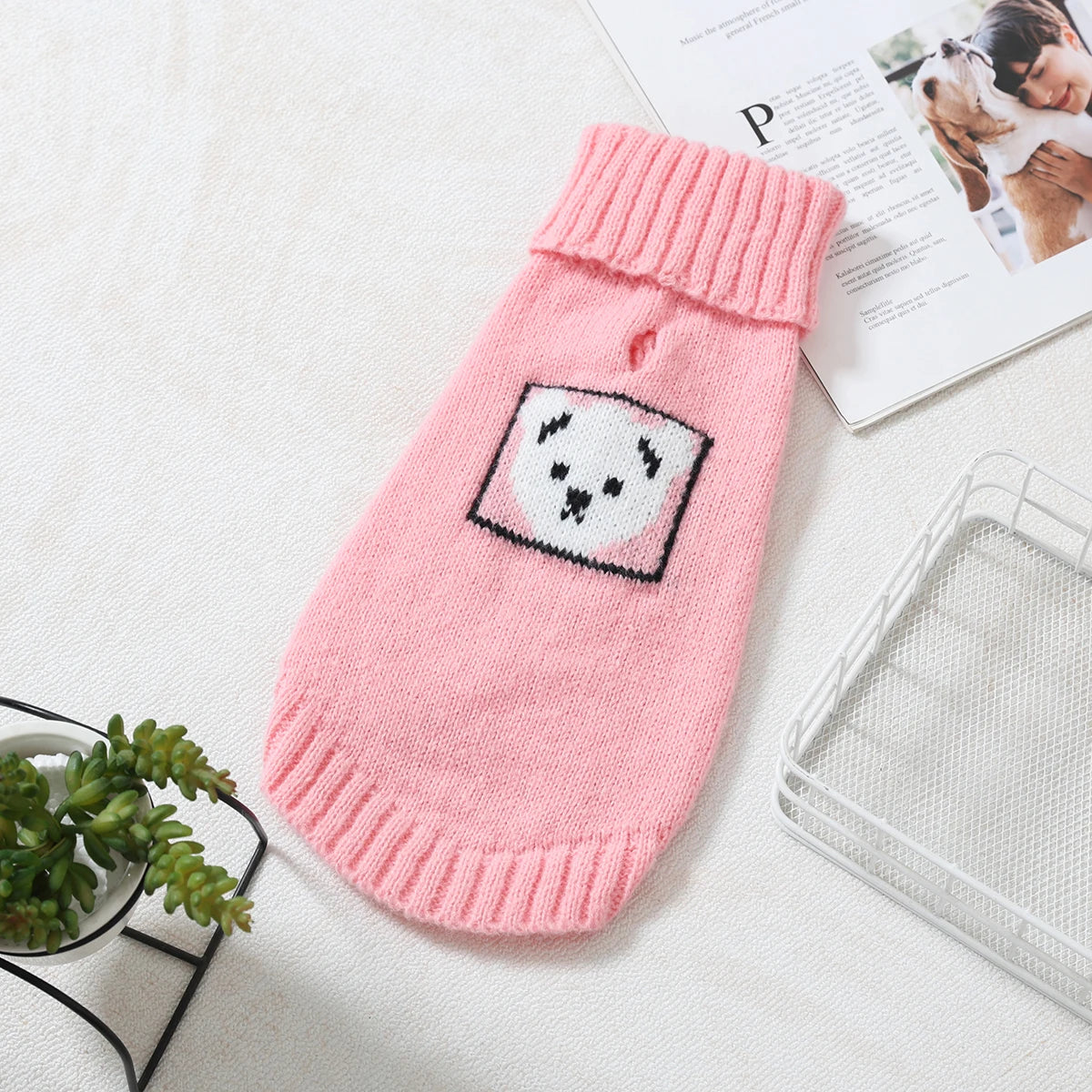 A pink knitted sweater for a small dog with a white paw print design, resting on a white surface.