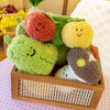 A wooden box filled with soft plush vegetable dolls including a red peanut, green broccoli, and yellow mushroom.