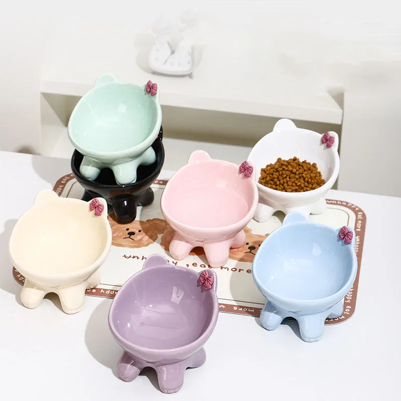A collection of light colored ceramic cat food bowls with raised and tilted designs, including pink, mint green, and blue.