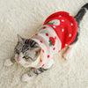 A tabby cat wearing a festive red knitted sweater with white polka dots and a red floral design, lying on a white fluffy surf