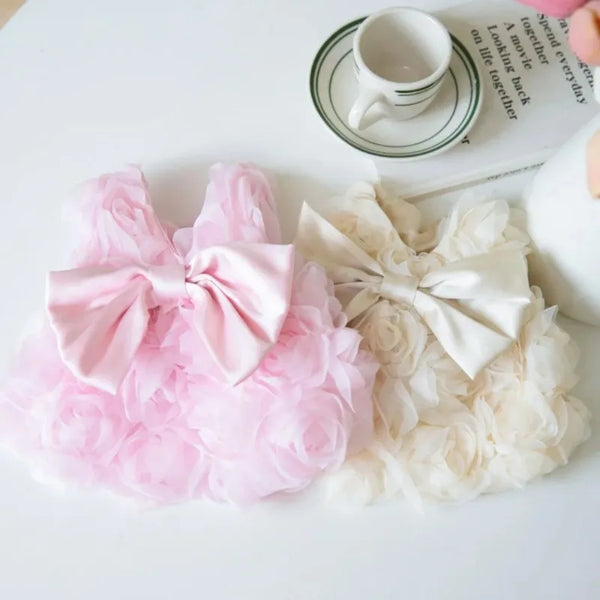Pink and cream floral pet dresses displayed next to a cup and a notebook.