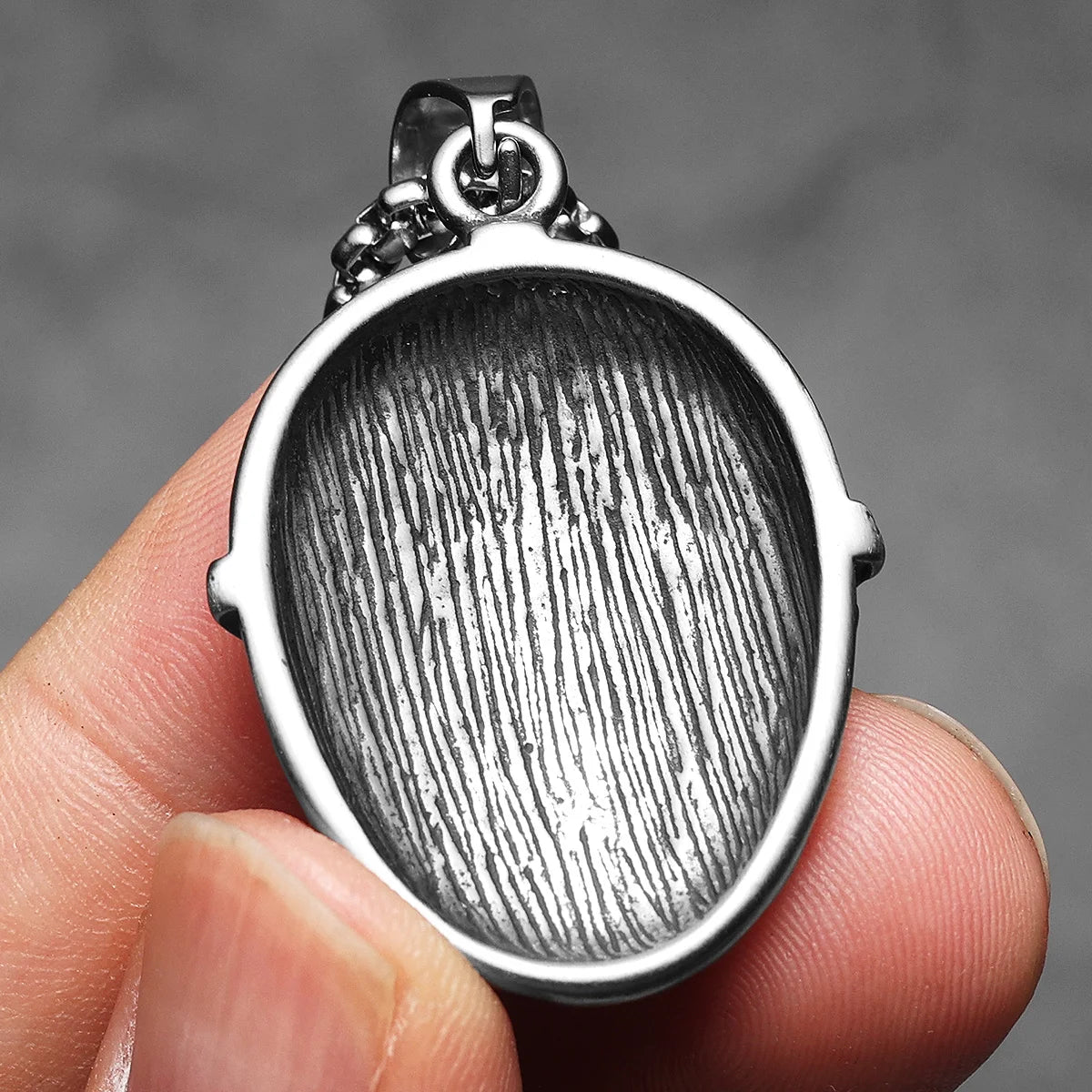 A silver stainless steel Jason Mask pendant necklace is held in a hand against a gray background.