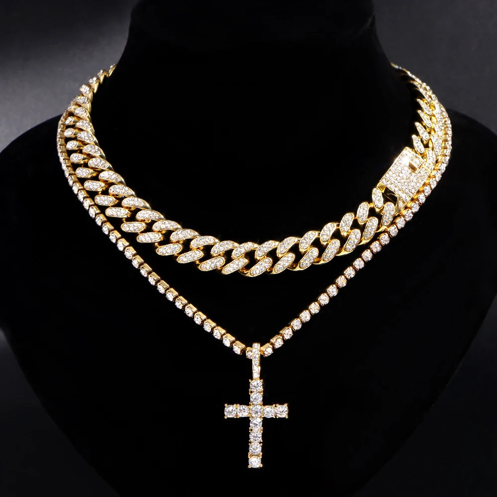 A gold-toned diamond Cuban link necklace set featuring a layered chain and a cross pendant displayed on a black velvet displa