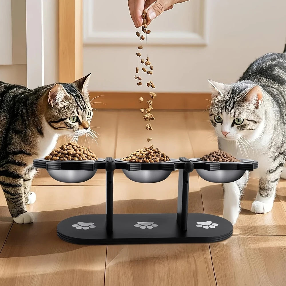 A hand is pouring cat food into three stainless steel bowls mounted on a black stand for elevated feeding.