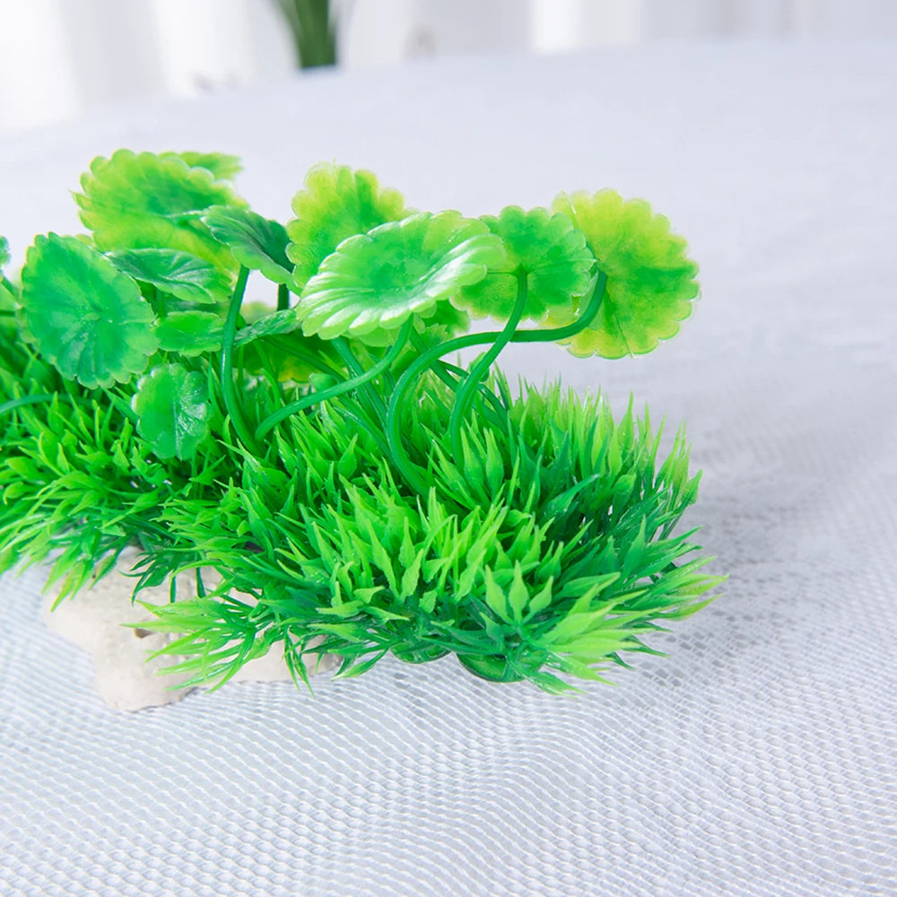 Planta de acuario artificial con hojas verde brillante creciendo desde una base de cerámica sobre una superficie blanca.
