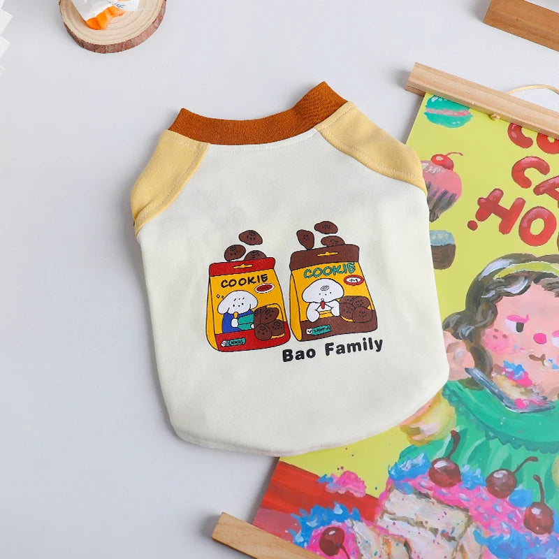 A cream-colored dog vest t-shirt with a yellow collar and a graphic featuring cookies and the text Bao Family.