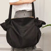 A black foldable travel organizer bag is shown being held by a person wearing a checkered skirt.