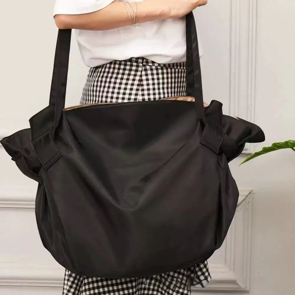 A black foldable travel organizer bag is shown being held by a person wearing a checkered skirt.