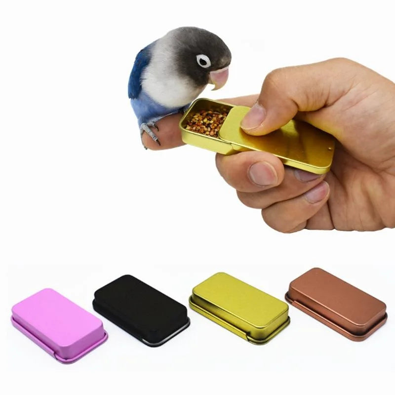 A hand holds a gold-colored parrot training treat dispenser, with a small dove perched nearby.