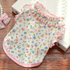 Pink floral vest for dogs and cats with ruffled trim shown on a wooden surface.