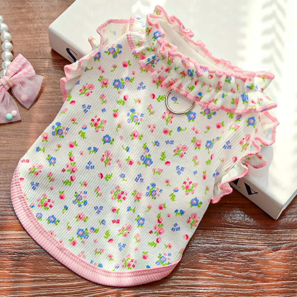 Pink floral vest for dogs and cats with ruffled trim shown on a wooden surface.