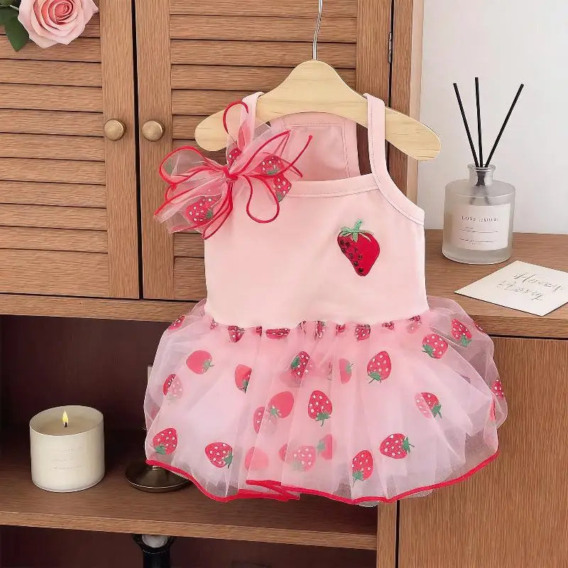 A pink strawberry princess pet dress with a floral bow hanging on a wooden hanger.