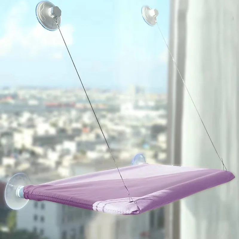 Lit hamac à ventouse violet suspendu par de fines ficelles, vu de dessus contre un panorama de ville.