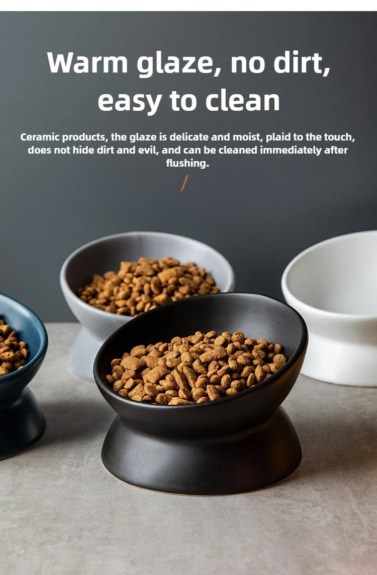 A black ceramic cat bowl with a raised stand filled with dry kibble, displayed on a gray surface.