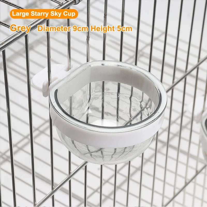 A grey large starry sky cup bird feeder with a transparent window hanging in a wire cage.
