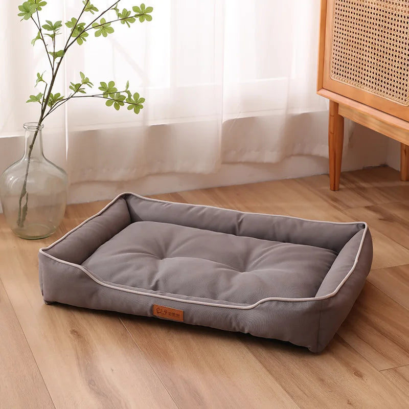 A gray corduroy pet sofa bed for dogs and cats resting on a wooden floor next to a vase of greenery.