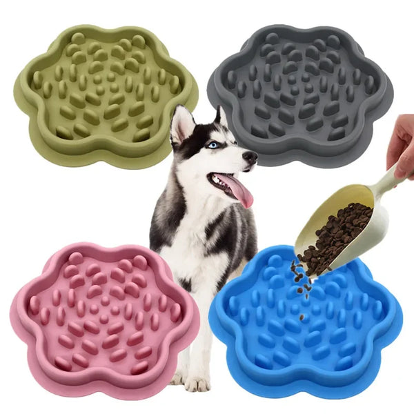 A white dog is standing next to silicone slow-feed pet mats in green, gray, pink, and blue colors.