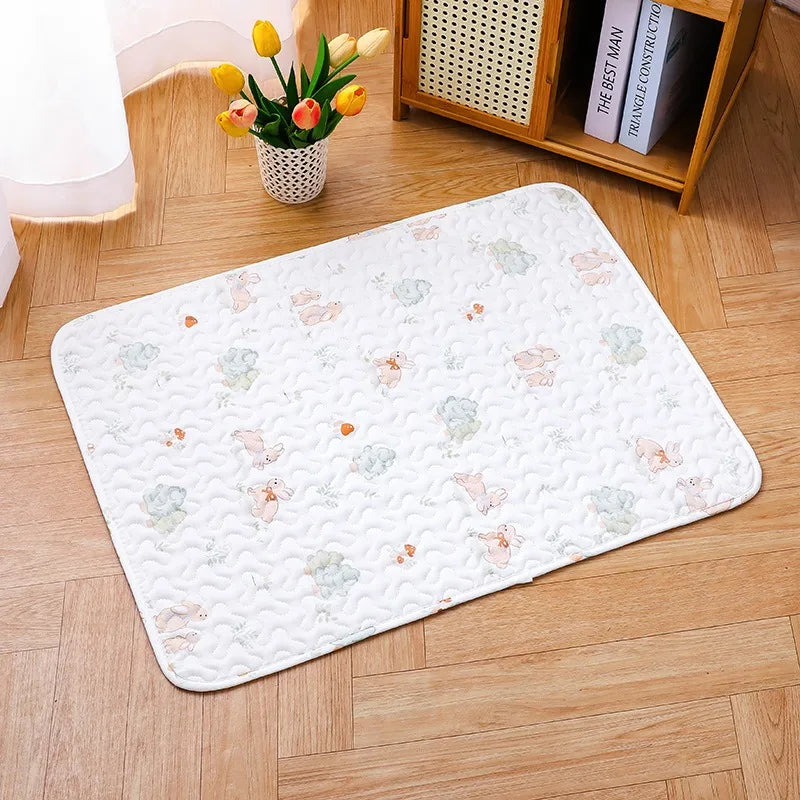 A white quilted pet cage mat with a non-slip base placed on a light wood floor.