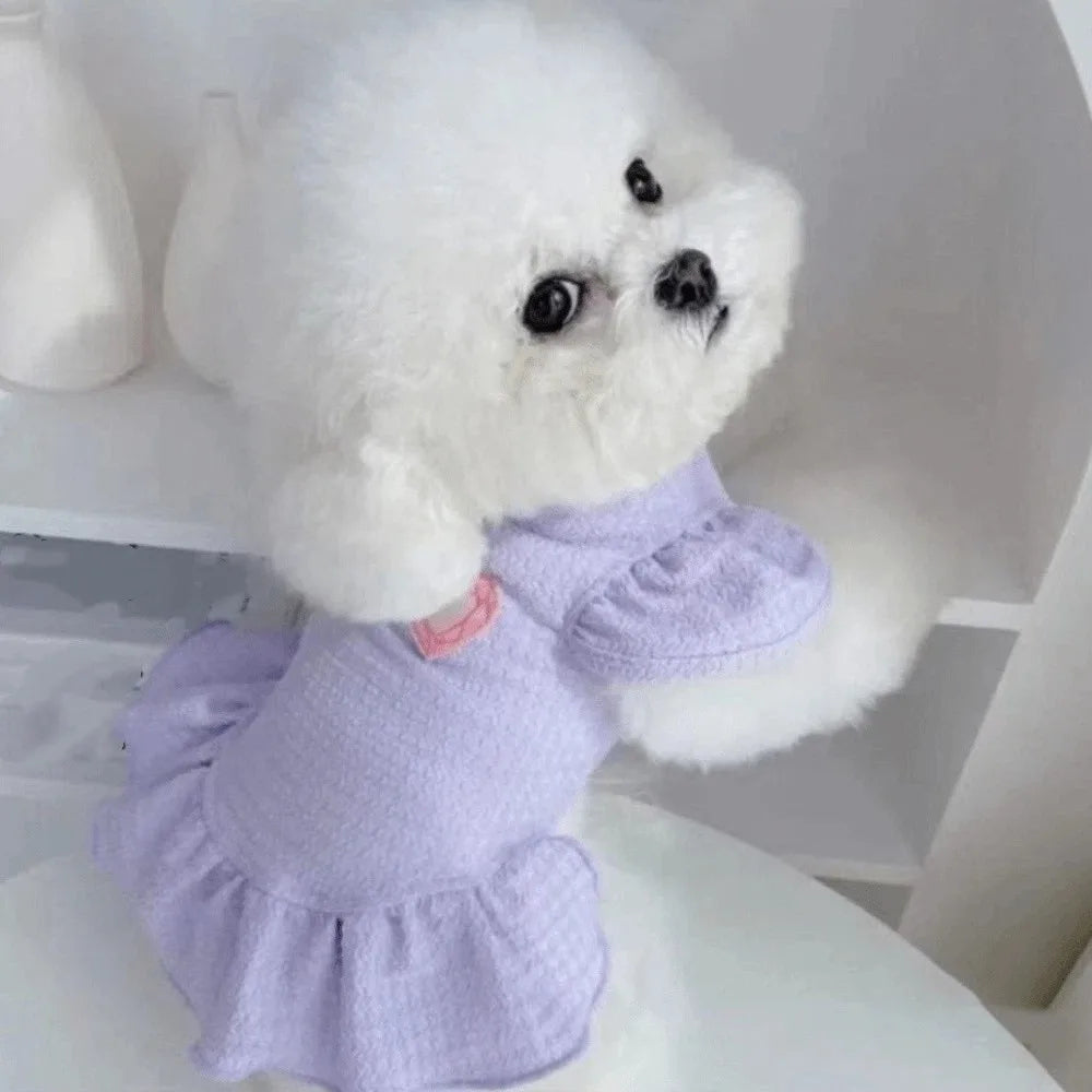 A white fluffy dog doll wearing a lavender dress with flutter sleeves.