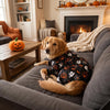 A golden retriever wearing a black and orange Halloween-themed pajama costume relaxing on a gray sofa.