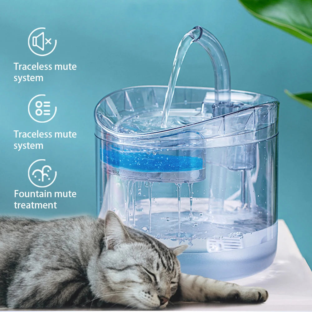 A cat is resting near a clear water fountain device with a transparent filter and a blue light.