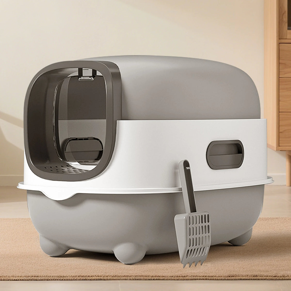 A gray enclosed stainless steel cat litter box with a removable tray and a metal scoop on a light carpet.