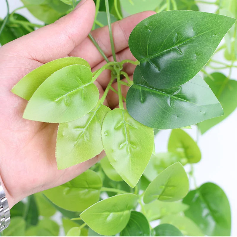 A hand holds a branch of artificial ivy plant with green leaves.