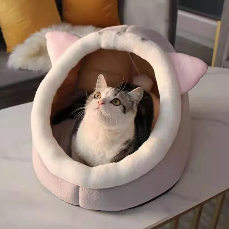 A fluffy gray and white cat is resting inside a soft, pink pet cave bed.